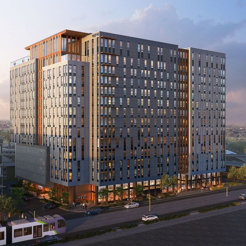 Exterior view of the high-rise VERVE Tempe building at dusk, showcasing modern architecture with floor-to-ceiling windows and warm lighting along the street level.