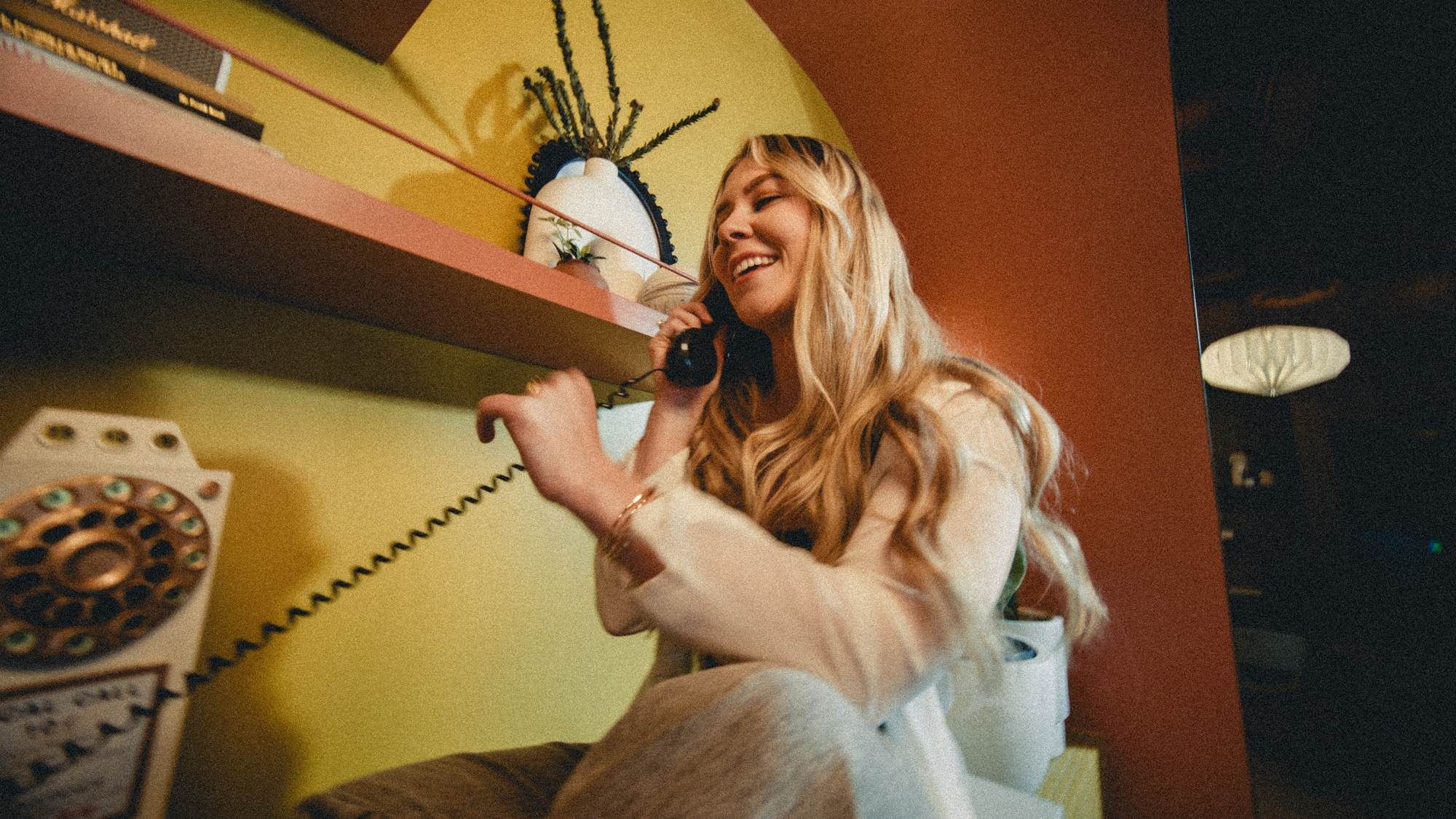 A smiling resident chats on the phone in a vibrant lounge space at VERVE Tempe, surrounded by colorful walls and playful decor.