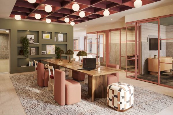 Study lounge at VERVE Tempe with a long wooden table, plush pink chairs, and geometric ottoman. The space features soft lighting, built-in shelving, and a cozy, modern design ideal for focused work or collaboration.
